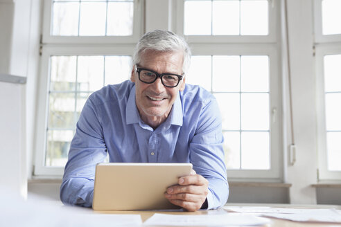 Porträt eines lächelnden reifen Geschäftsmannes am Bürotisch, der ein Tablet hält - RBF005051