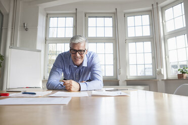 Portrait of confident mature businessman leaning on table in conference room - RBF005055