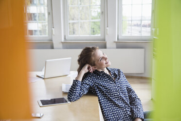 Lächelnde Frau im Büro, die sich auf einen Tisch stützt - RBF005069