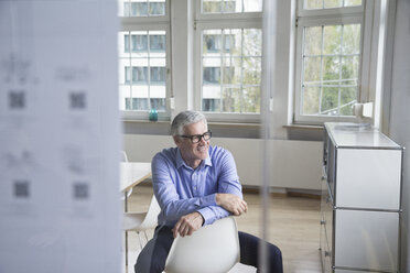 Smiling mature businessman sitting on chair in office - RBF005070