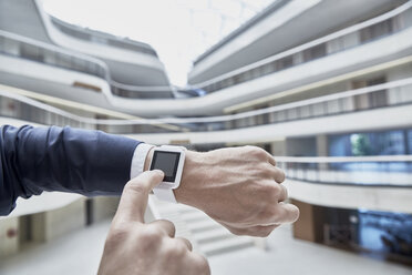 Businessman touching smartwatch in office building - FMKF002890