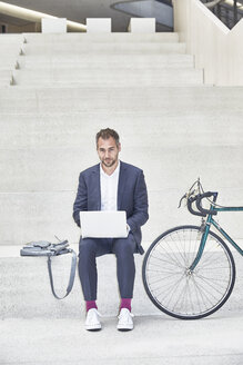 Geschäftsmann auf der Treppe mit Laptop neben dem Fahrrad - FMKF002900