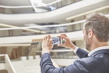 Businessman taking cell phone picture in modern office building - FMKF002901