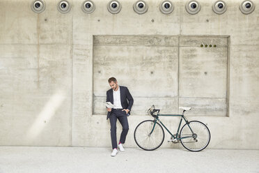 Geschäftsmann mit Fahrrad an Betonwand, der ein Dokument liest - FMKF002903