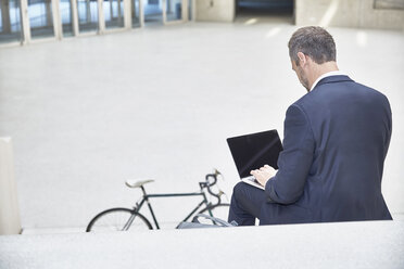 Businesssman on stairs using laptop - FMKF002904