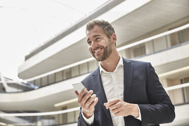 Smiling businessman in office building holding cell phone - FMKF002908