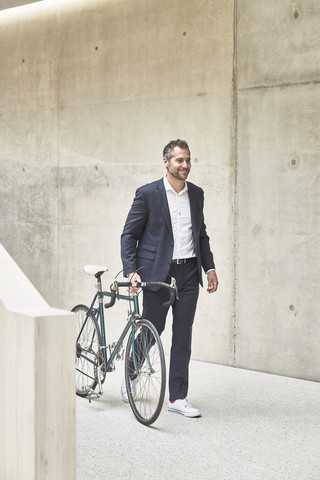 Geschäftsmann schiebt Fahrrad an Betonwand entlang, lizenzfreies Stockfoto