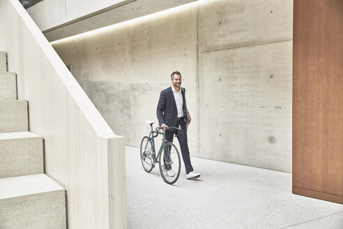 Businesssman pushing bicycle along concrete wall - FMKF002916