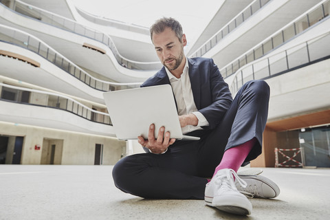 Businesssman sitting on floor in office building using laptop stock photo