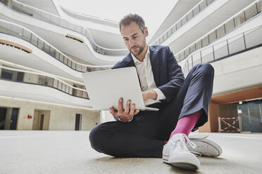 Geschäftsmann sitzt auf dem Boden in einem Bürogebäude und benutzt einen Laptop - FMKF002927