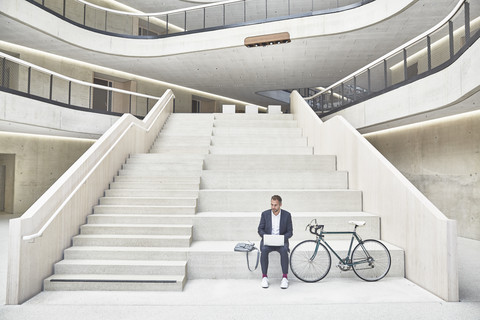 Businesssman on stairs using laptop next to bicycle stock photo