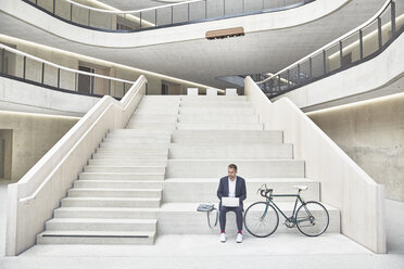 Geschäftsmann auf der Treppe mit Laptop neben dem Fahrrad - FMKF002929