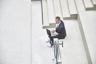 Geschäftsmann auf der Treppe mit Laptop neben dem Fahrrad - FMKF002931