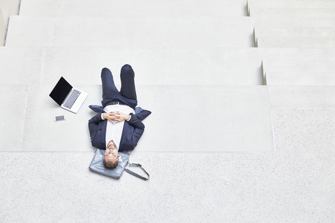Businesssman lying on stairs next to laptop and cell phone stock photo