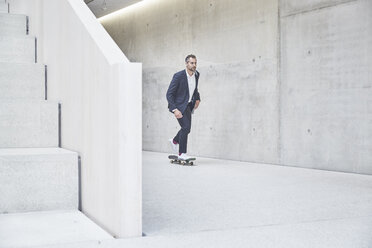 Businesssman riding skateboard along concrete wall - FMKF002945