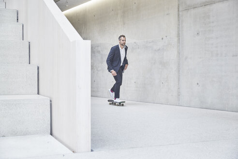 Geschäftsmann fährt mit dem Skateboard an einer Betonwand entlang - FMKF002945