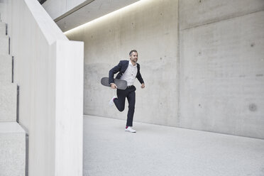 Businesssman running with skateboard along concrete wall - FMKF002948