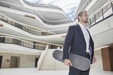Businesssman standing with skateboard in office building - FMKF002949