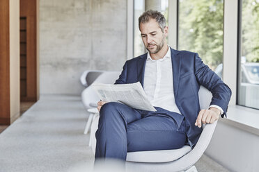 Businesssman sitting on chair reading newspaper - FMKF002954