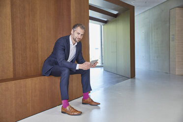 Businessman sitting on wooden ledge holding tablet - FMKF002963