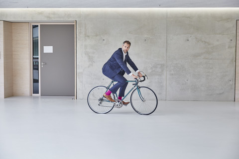 Businesssman riding bicycle in office building stock photo