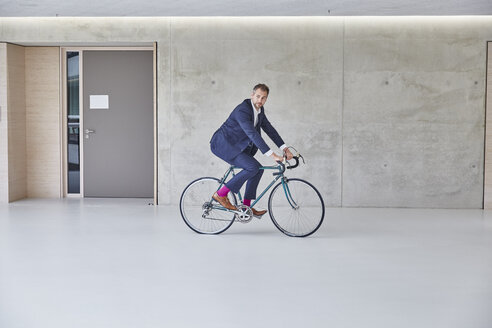 Geschäftsmann fährt Fahrrad im Bürogebäude - FMKF002966