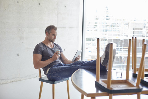 Mann benutzt Tablet am Tisch mit Stühlen darauf, lizenzfreies Stockfoto