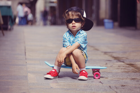 Porträt eines kleinen Jungen, der auf einem Skateboard sitzt und eine übergroße Sonnenbrille und ein Basecap trägt - XCF000097