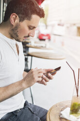 Mann sitzt in einem Straßencafé und benutzt sein Smartphone - JUNF000613