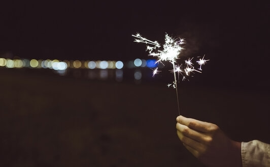 Man's hand holding sparkler on the beach at night - DAPF000297