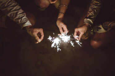 Hands of three friends holding sparklers on the beach at night - DAPF000298