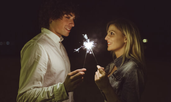 Young couple in love holding sparklers on the beach at night - DAPF000299