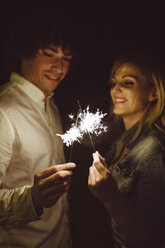 Young couple in love holding sparklers on the beach at night - DAPF000301