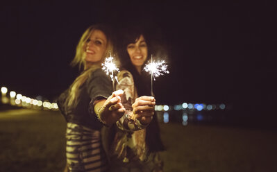 Two happy friends holding sparklers on the beach at night - DAPF000303