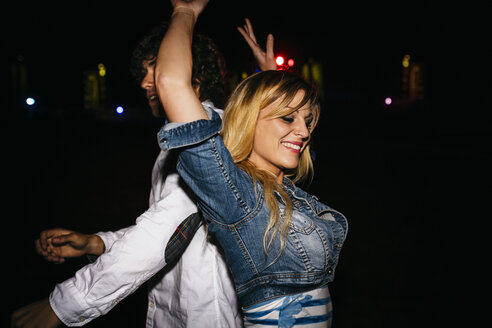Glückliche junge Frau tanzt Rücken an Rücken mit einem Mann auf einem Sommernachtsfest - DAPF000306