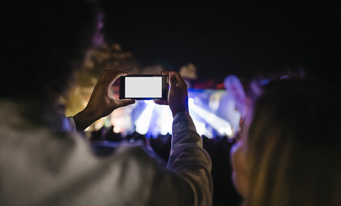 Rückansicht eines jungen Mannes, der bei einem Sommerkonzert Fotos mit seinem Smartphone macht, lizenzfreies Stockfoto