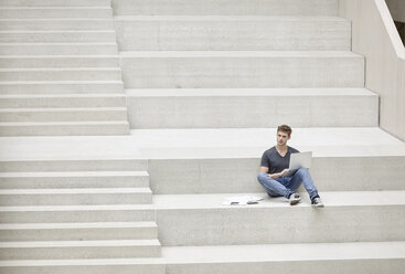 Junger Mann sitzt auf einer Treppe und benutzt einen Laptop - FMKF002974