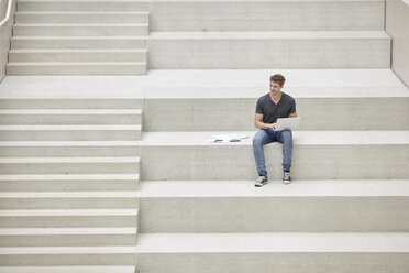 Junger Mann sitzt auf einer Treppe und benutzt einen Laptop - FMKF002975