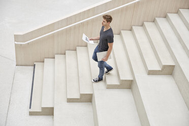 Young man with laptop and documents walking on stairs - FMKF002988
