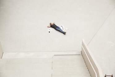 Junger Mann auf dem Boden liegend, umgeben von Papieren - FMKF002994