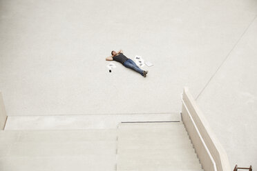 Young man lying on floor surrounded by papers - FMKF002994