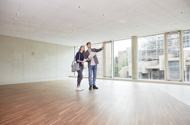 Young man and woman with documents talking in empty room - FMKF003012