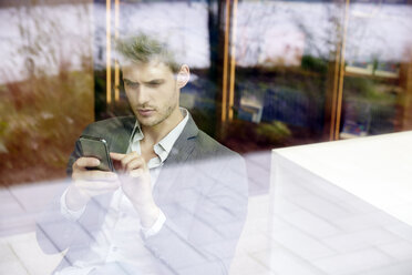 Junger Mann benutzt Mobiltelefon in der Bibliothek - FMKF003015