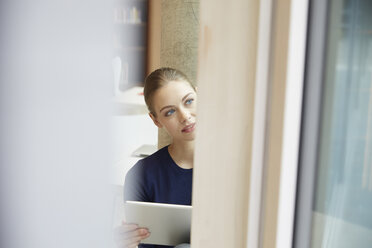 Young woman holding tablet looking out of window - FMKF003019