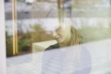 Junge Frau mit Tablet hinter Fensterscheibe - FMKF003020