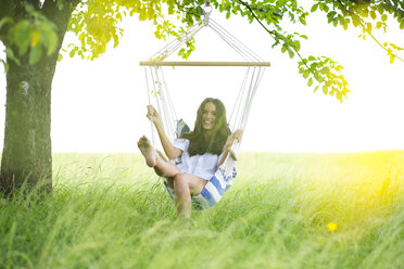 Happy woman relaxing in a hanging chair under a tree - MAEF011944