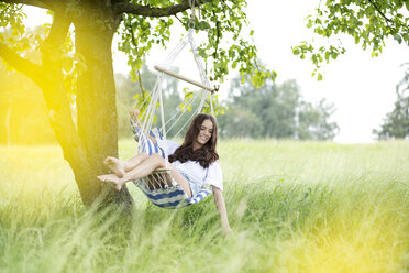 Happy woman relaxing in a hanging chair under a tree - MAEF011952