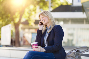 Lächelnde blonde Geschäftsfrau mit Kaffee zum Mitnehmen am Telefon - NAF000021