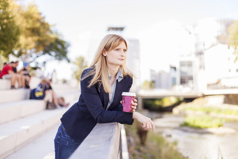Geschäftsfrau mit Kaffee zum Mitnehmen lehnt am Geländer und schaut in die Ferne - NAF000027
