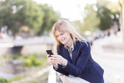 Smiling businesswoman leaning on railing looking at cell phone stock photo